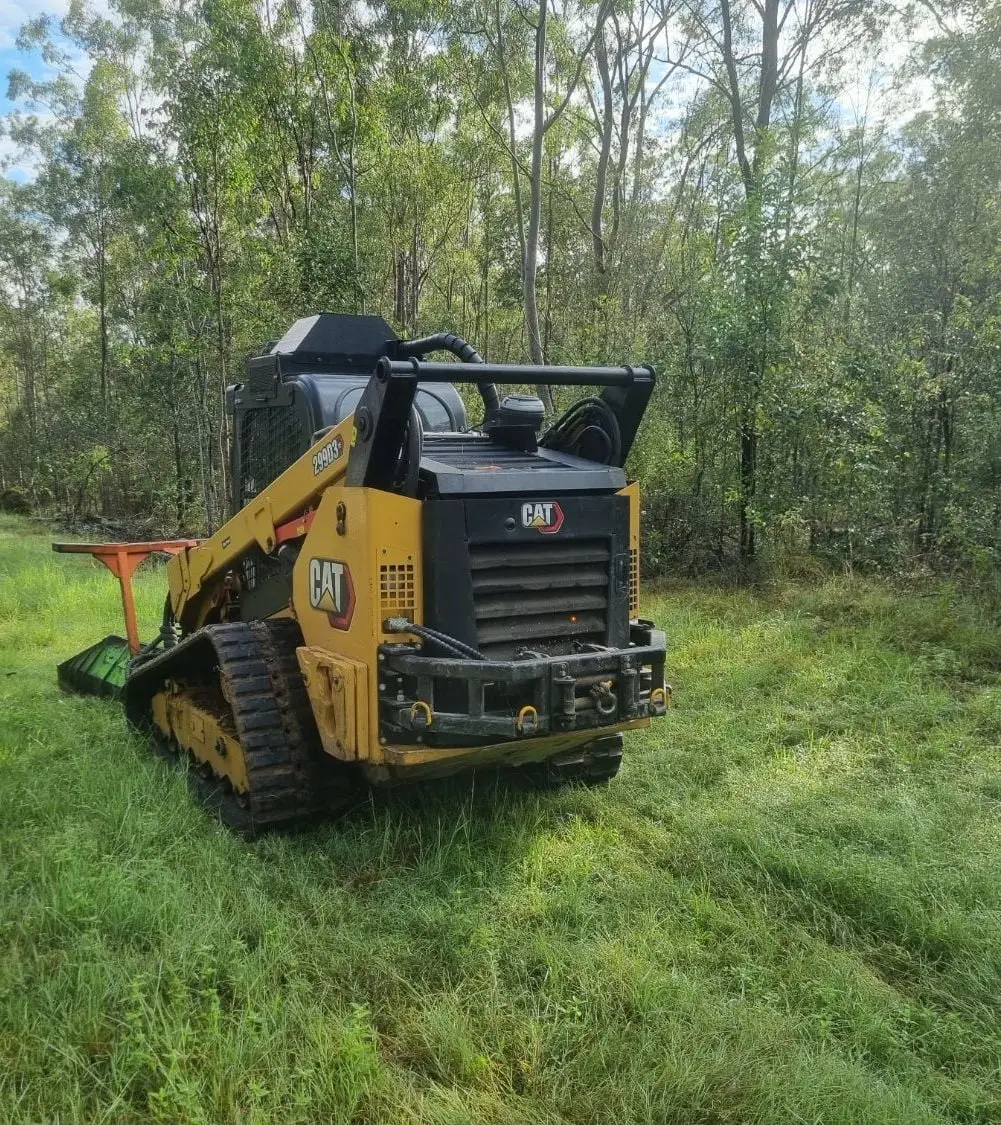 A tracked forestry mulcher parked on fresh green grass at the edge of thick bush